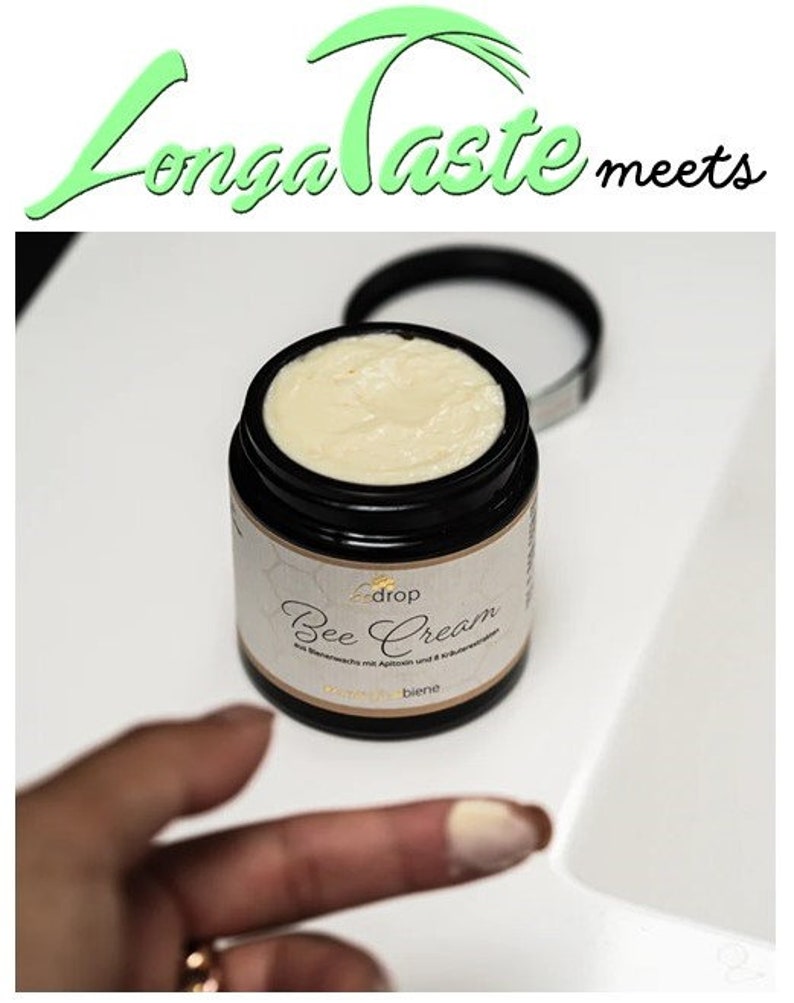 May include: A black jar of Bee Cream with a white label and a light beige cream inside. The jar is open, and the lid is next to it. The text "Longa Taste meets" is above the jar in green and black.