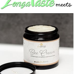 May include: A black jar of "Bee Cream" with a white label and a black lid. The label includes the brand name "bedrop" and the words "Bee Cream" in cursive. The jar is open, revealing the cream inside. The text "Longa Taste meets" is at the top.