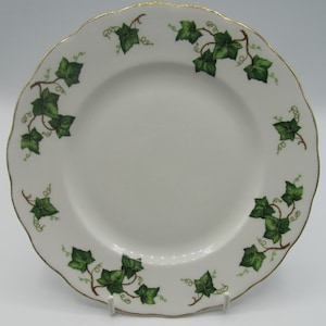 May include: A white ceramic plate with a gold rim and a green ivy design. The plate has a scalloped edge.