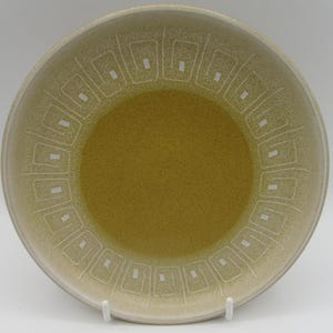 May include: A large, round, beige ceramic bowl with a geometric pattern of white squares around the rim.