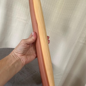 May include: A cylindrical wooden rolling pin featuring a distinct color contrast between a deep reddish-brown section and a lighter cream-colored section. The surface of the kitchen tool is smooth and polished, showing the natural grain of the wood.