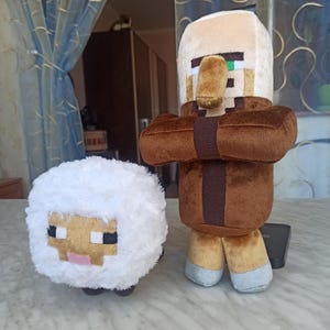 May include: Two plush toys: a white sheep with a pixelated face and a brown and tan Minecraft villager. The sheep has a fluffy body and black, pink, and tan details. The villager has a brown robe, tan face, and pixelated features.