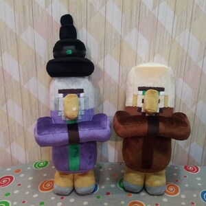 May include: Two plush Minecraft character dolls. One doll is dressed in purple with a black hat, the other in brown. Both dolls have tan noses and are holding their hands together in front of them. The dolls are on a patterned surface.