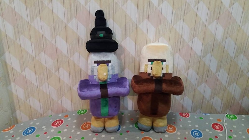 May include: Two plush Minecraft character dolls. One doll is dressed in purple with a black hat, the other in brown. Both dolls have tan noses and are holding their hands together in front of them. The dolls are on a patterned surface.