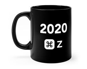 May include: A black ceramic mug featuring the white text 2020 positioned above a white command key symbol and the letter Z. The mug has a curved handle on the left side and a smooth, glossy finish, presenting a simple and functional design.