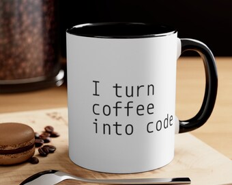 May include: A white ceramic mug with a black interior and a black handle. The exterior features the black printed text "I turn coffee into code" in a simple sans-serif font. The mug is positioned upright with a smooth, cylindrical body.