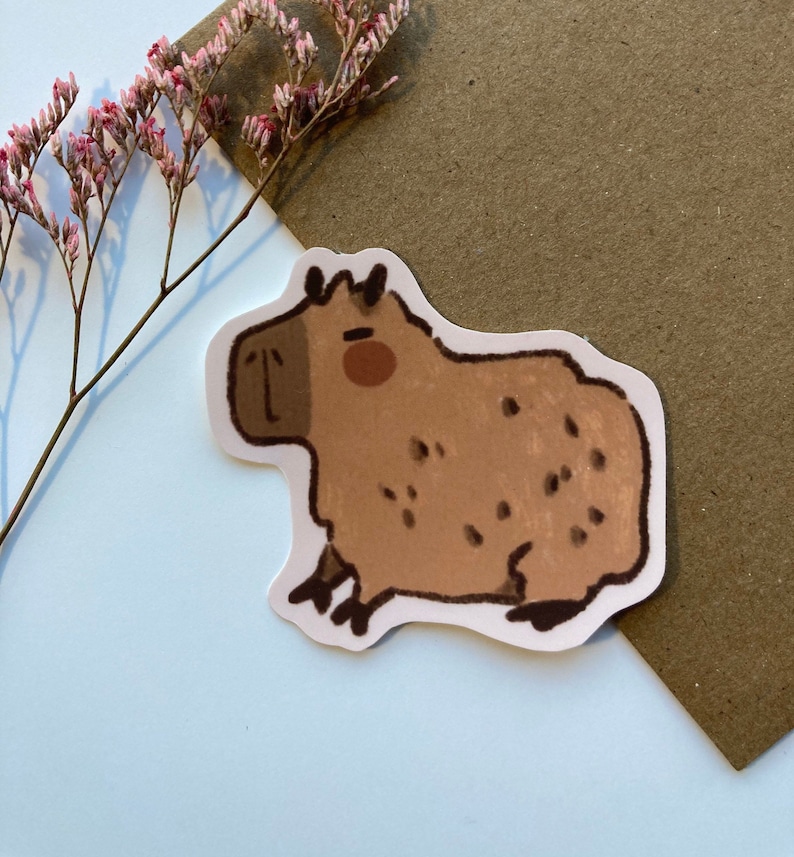 May include: A brown and white capybara sticker with a cartoon-like style. The capybara has a brown body with white spots and a white face with brown eyes and a pink nose.