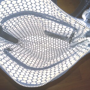 May include: Black handbag with a patterned interior. The interior features a white and black polka dot design. The bag has multiple zippered compartments and a black leather strap. The bag is open, revealing the interior.