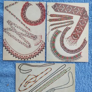 May include: Three vintage postcards showcasing colorful beaded jewelry designs. The cards feature necklaces, bracelets, and decorative bands with intricate patterns in red, white, green, and yellow. The designs are displayed on a cream-colored background.