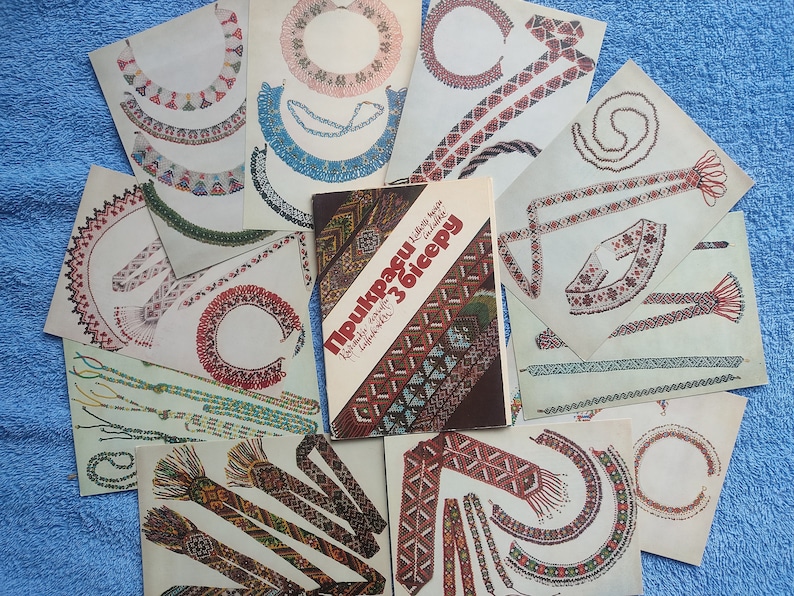 May include: A collection of printed designs for beaded jewelry, including necklaces and bracelets, with a book titled "Прикраси з бісеру" in the center. The designs feature various patterns and colors, showcasing traditional beadwork.