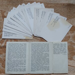 May include: A collection of blank white postcards with a folded pamphlet containing text in Russian. The pamphlet is open and the text is visible. The postcards and pamphlet are on a brown textured surface.