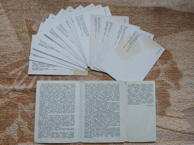 May include: A collection of blank white postcards with a folded pamphlet containing text in Russian. The pamphlet is open and the text is visible. The postcards and pamphlet are on a brown textured surface.