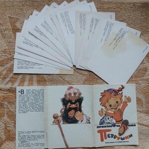 May include: A vintage book titled "Приключения Петрушки" (Adventures of Petrushka) with illustrations of a bearded man in a crown and a red-haired boy with a dog. The book is open to reveal the text and illustrations. There are also 15 blank postcards in the background.