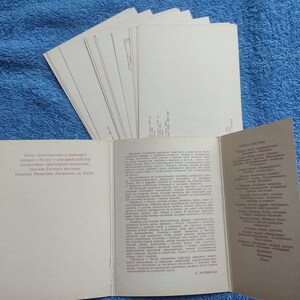 May include: A collection of vintage postcards and a brochure with text in a foreign language, likely Ukrainian, are displayed on a blue textured surface. The postcards are stacked, while the brochure is open, revealing printed content.