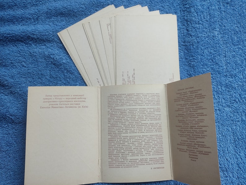 May include: A collection of vintage postcards and a brochure with text in a foreign language, likely Ukrainian, are displayed on a blue textured surface. The postcards are stacked, while the brochure is open, revealing printed content.