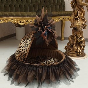 May include: A brown and black leopard print pet bed with a brown tulle skirt and a brown bow on top.