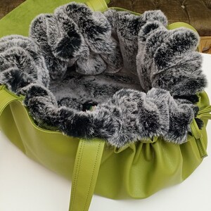 May include: A green leather tote bag with a black and grey faux fur lining. The bag has two straps and a drawstring closure.