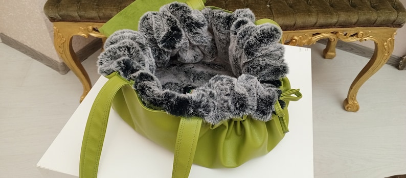 May include: A green leather tote bag with a black and grey faux fur lining. The bag has two straps and a drawstring closure.