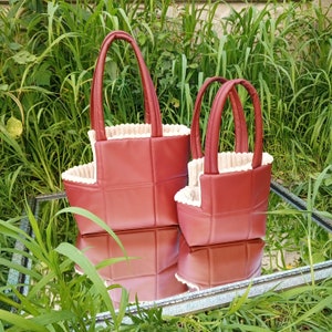 May include: Two red quilted tote bags with cream trim. The larger bag has two handles and the smaller bag has one handle.