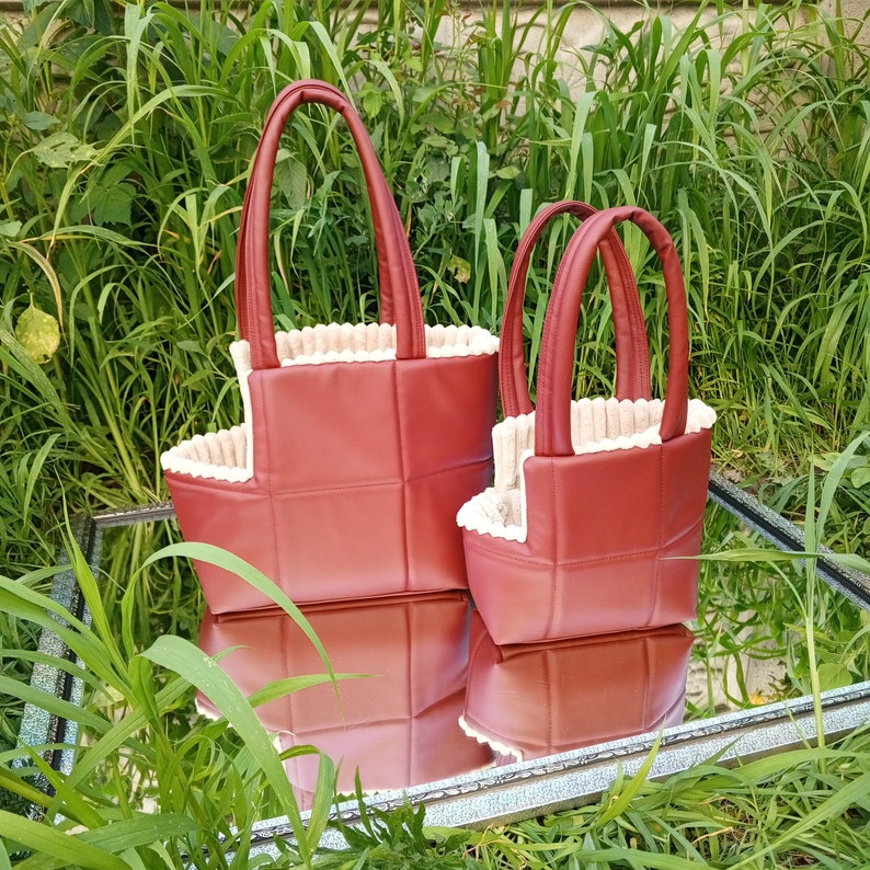 May include: Two red quilted tote bags with cream trim. The larger bag has two handles and the smaller bag has one handle.