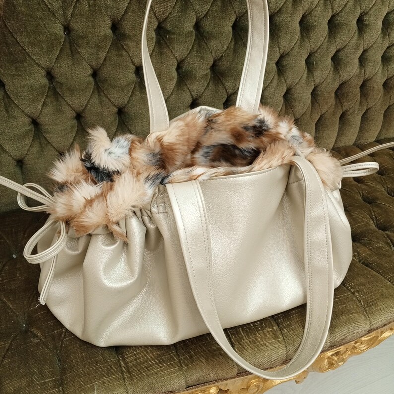 K&ouml;nnte beinhalten: Eine goldene Tasche aus Kunstleder mit einem flauschigen braunen und wei&szlig;en Kunstfellfutter. Die Tasche hat zwei lange Henkel und einen Kordelzug.