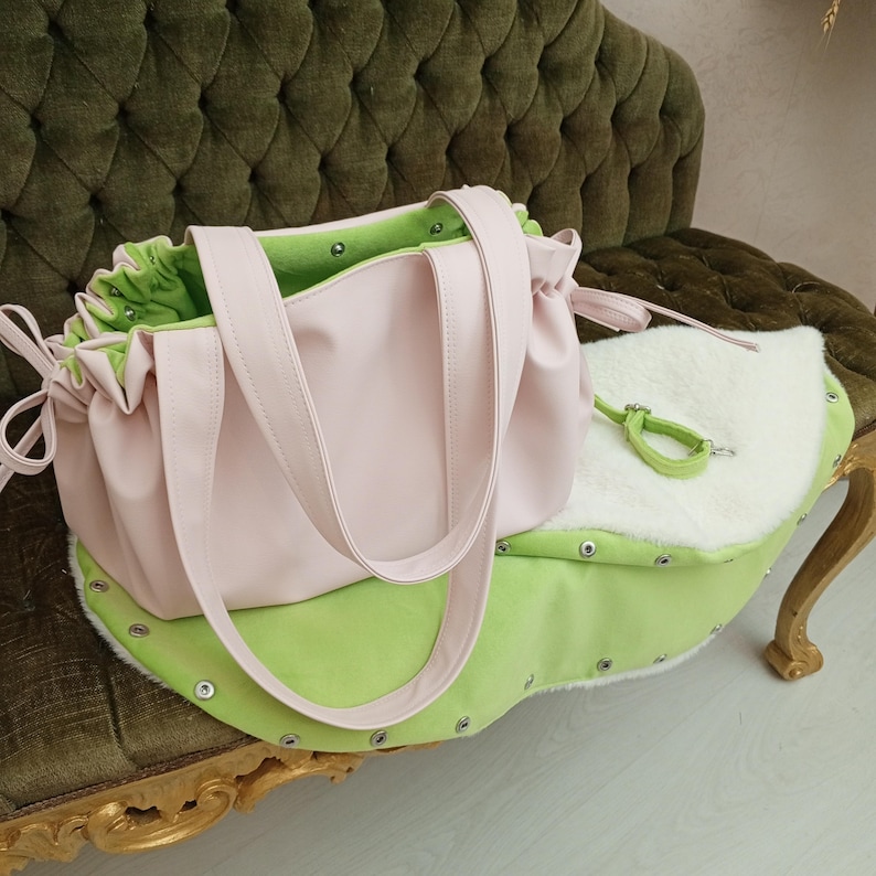 May include: A light pink tote bag with matching straps and a green interior sits atop a green and white pet bed. The pet bed has a light green exterior and a white, fluffy interior. A green leash is attached to the bed.