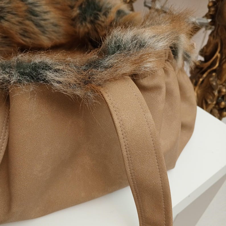 Pu&ograve; includere: Una borsa tote marrone con un bordo in pelliccia sintetica marrone e manici marroni. La borsa &egrave; realizzata in un tessuto morbido e testurizzato.