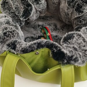 May include: A green leather tote bag with a black and grey faux fur lining. The bag has two handles and a zip closure.