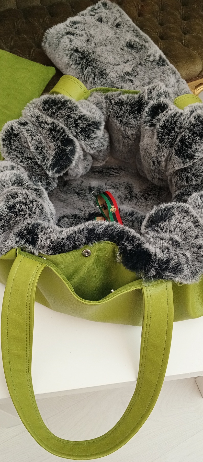 May include: A green leather tote bag with a black and grey faux fur lining. The bag has two handles and a zip closure.