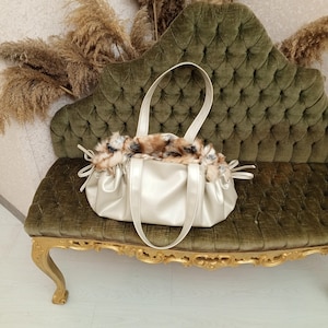 K&ouml;nnte beinhalten: Eine goldfarbene Handtasche mit einem Futter aus Kunstpelz. Die Tasche hat zwei obere Henkel und ein gerafftes, gekr&auml;useltes Design.