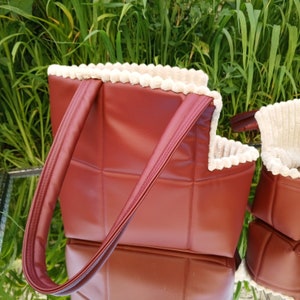 May include: A burgundy quilted tote bag with a white faux fur trim. The bag has two handles and a zipper closure.