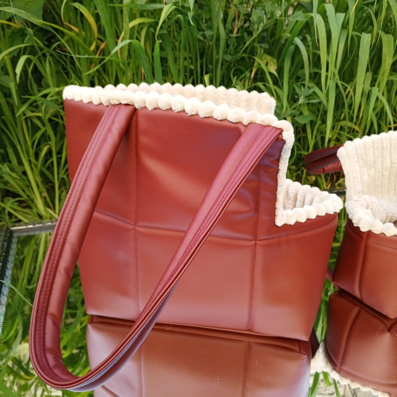 May include: A burgundy quilted tote bag with a white faux fur trim. The bag has two handles and a zipper closure.