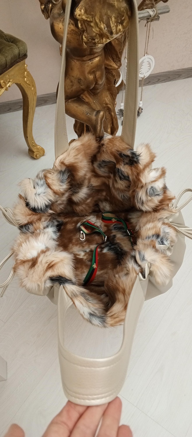 K&ouml;nnte beinhalten: Eine beige Tasche mit Kunstfellfutter und einem langen Trageriemen. Die Tasche ist offen und das Futter ist sichtbar. Das Futter ist aus braunem und wei&szlig;em Kunstfell.