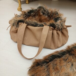 Pu&ograve; includere: Una borsa tote in similpelle marrone con rifiniture in pelliccia sintetica marrone e nera. La borsa ha due manici e una parte superiore arricciata.