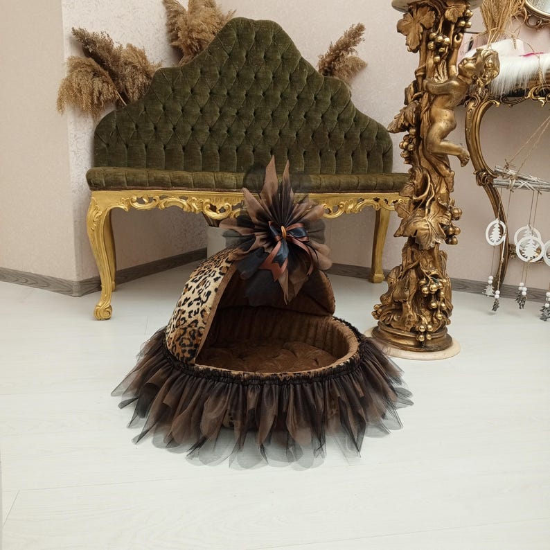 May include: A brown and black leopard print pet bed with a black tulle skirt and a brown bow. The bed has a soft brown lining and a removable hood.