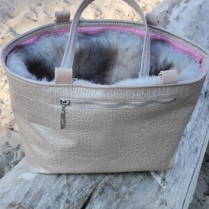 May include: A beige faux leather tote bag with a zipper closure and a furry lining. The bag has two top handles and a crocodile-embossed pattern.