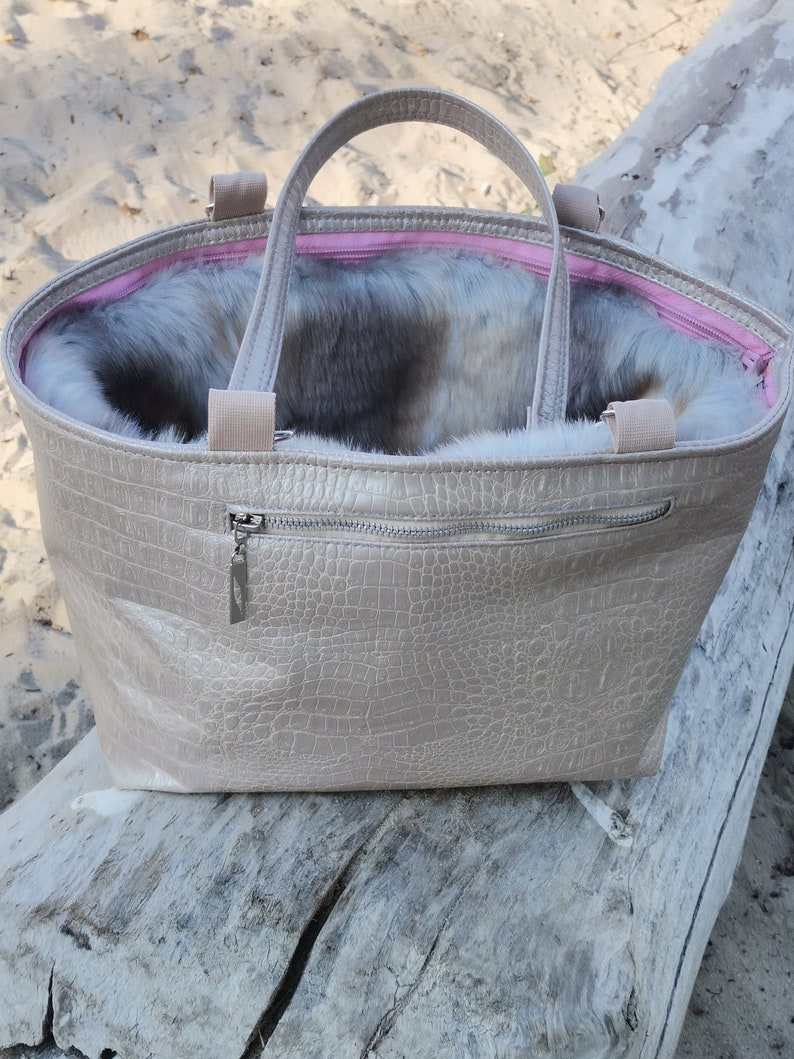May include: A beige faux leather tote bag with a zipper closure and a furry lining. The bag has two top handles and a crocodile-embossed pattern.