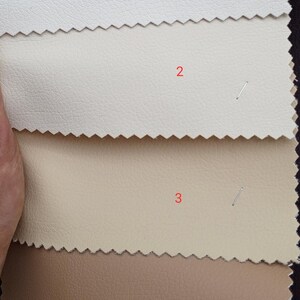 May include: A selection of four leather swatches in varying shades. The colors range from off-white to light beige, tan, and a medium brown. Each swatch is labeled with a number and has a textured surface.