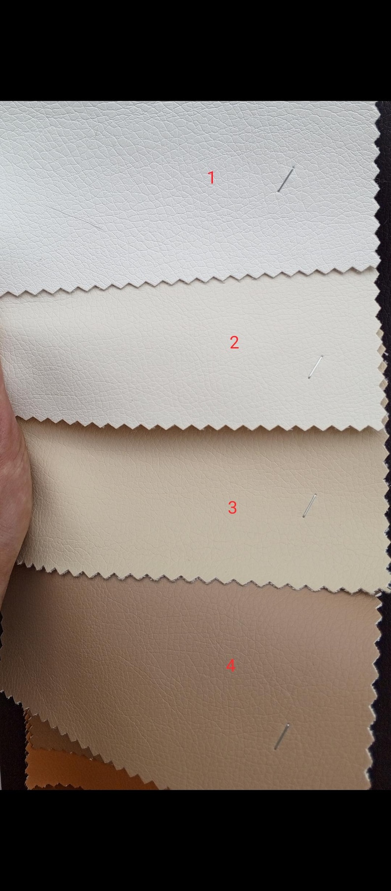 May include: A selection of four leather swatches in varying shades. The colors range from off-white to light beige, tan, and a medium brown. Each swatch is labeled with a number and has a textured surface.