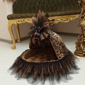 May include: A brown and black leopard print pet bed with a brown and black tulle skirt. The bed has a brown velvet lining and a brown bow with a black ribbon on top.