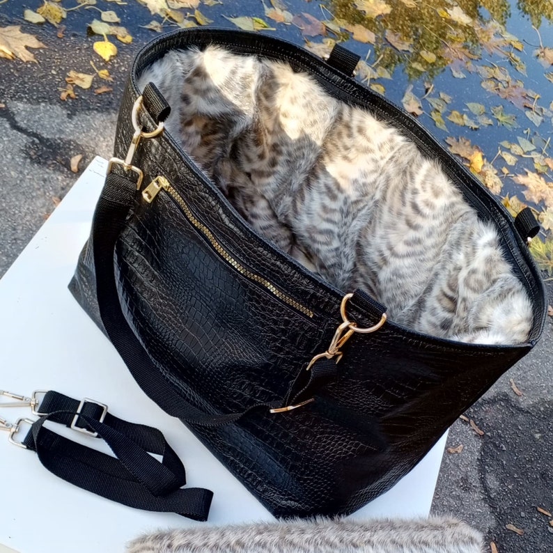 May include: A black leather tote bag with a faux fur lining. The bag has a zipper closure and two top handles. The bag also has a detachable shoulder strap.