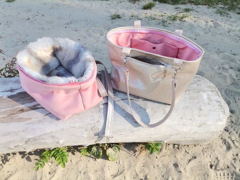 May include: Two pink and gold handbags with fur lining. One bag is open and shows a pink interior with a zippered pocket. The bags are sitting on a light brown log.