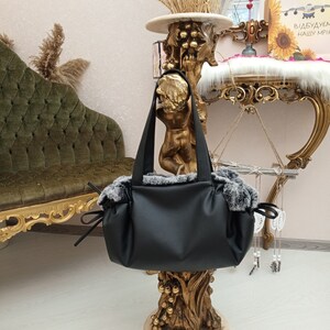 May include: A black faux leather tote bag with a grey faux fur trim. The bag has two top handles and a drawstring closure.