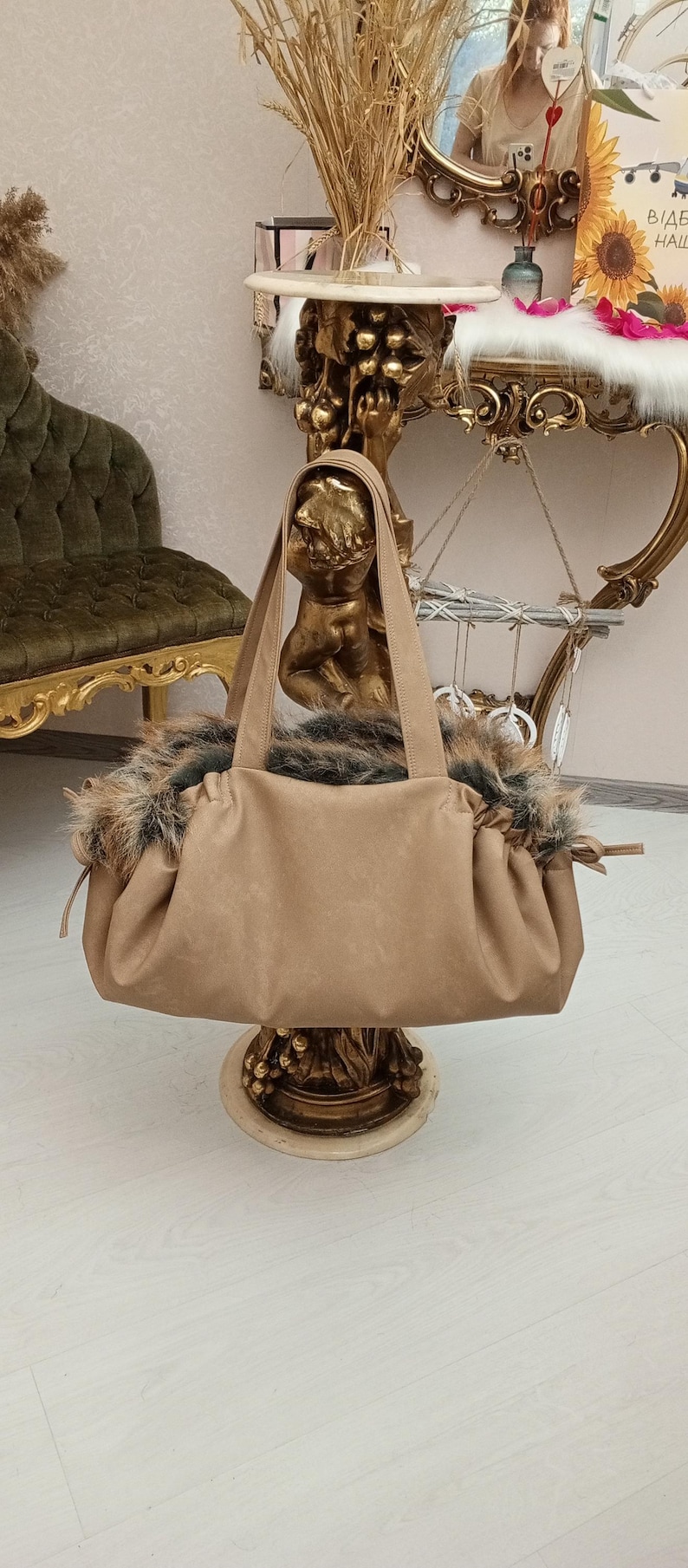Pu&ograve; includere: Una borsa tote in similpelle color beige con un bordo in pelliccia. La borsa &egrave; appoggiata su un piedistallo dorato.