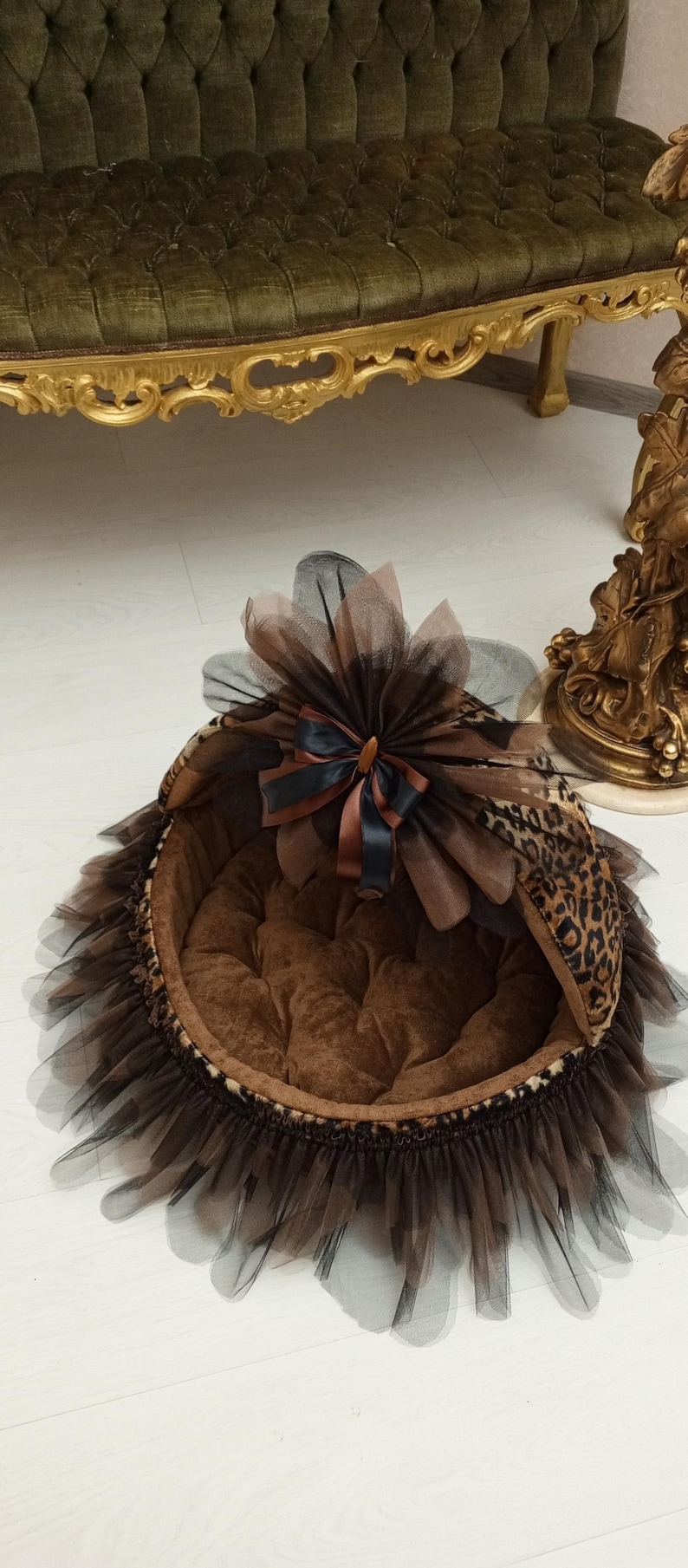 May include: A brown and black leopard print pet bed with a black tulle skirt and a brown and black bow. The bed has a brown velvet lining.