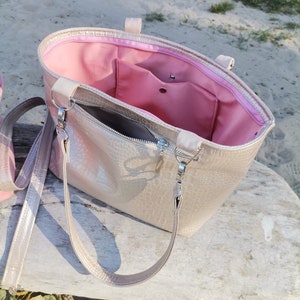 May include: A gold-colored tote bag with a pink lining and a zipper closure. The bag has a long strap and a shorter handle.