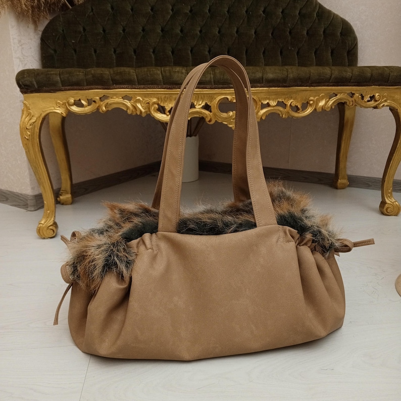 Pu&ograve; includere: Una borsa tote in pelle marrone con un bordo in pelliccia sintetica intorno alla parte superiore. La borsa ha due manici e una chiusura con coulisse.
