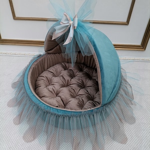 May include: A teal blue and brown pet bed with a tulle skirt and a bow on top. The bed has a soft, padded cushion inside.