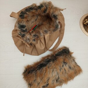 Pu&ograve; includere: Una borsa tote in similpelle marrone con una fodera in pelliccia sintetica marrone e nera soffice. La borsa ha una chiusura a coulisse e una tracolla lunga. &Egrave; inclusa anche una pochette in pelliccia sintetica abbinata.