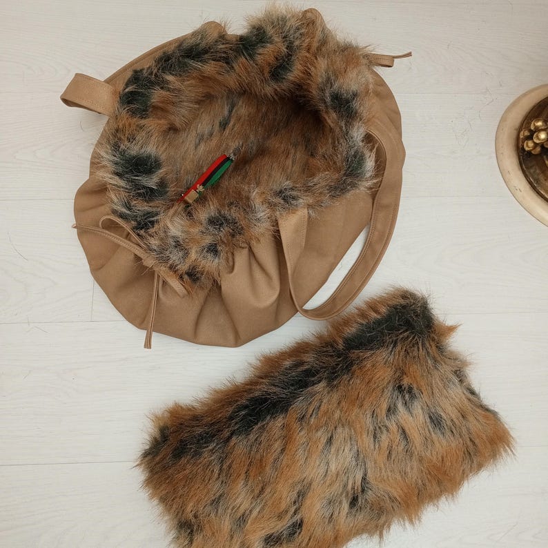 Pu&ograve; includere: Una borsa tote in similpelle marrone con una fodera in pelliccia sintetica marrone e nera soffice. La borsa ha una chiusura a coulisse e una tracolla lunga. &Egrave; inclusa anche una pochette in pelliccia sintetica abbinata.